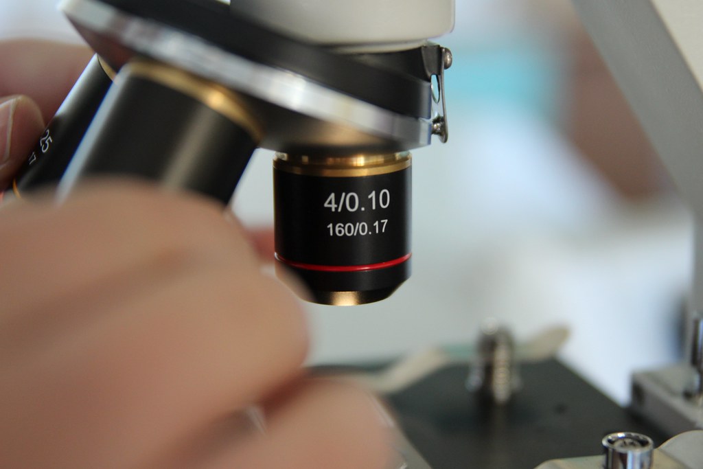 A closeup photo of a microscope in use, focusing on the lens of the microscope.
